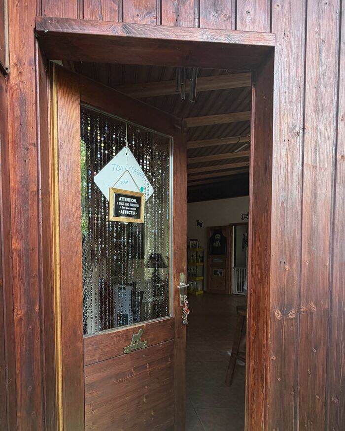 La porte d'entrée ouverte, rideau de perles et pancarte manuscrite sur la vitre.
