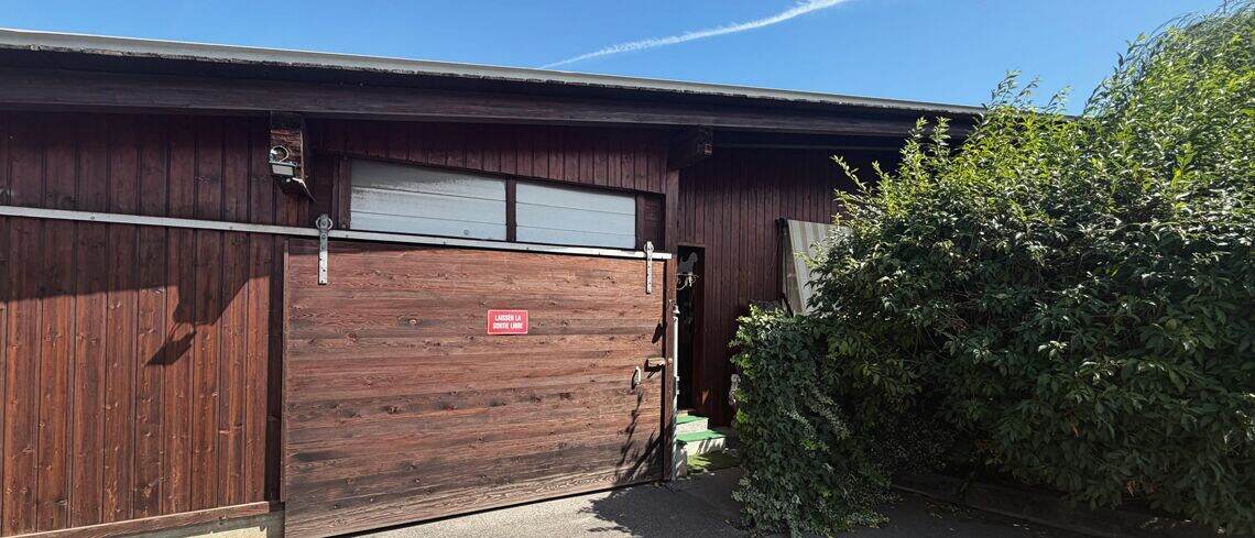 La façade du salon, bardage de bois brun, grande porte coulissante et panneau rouge.